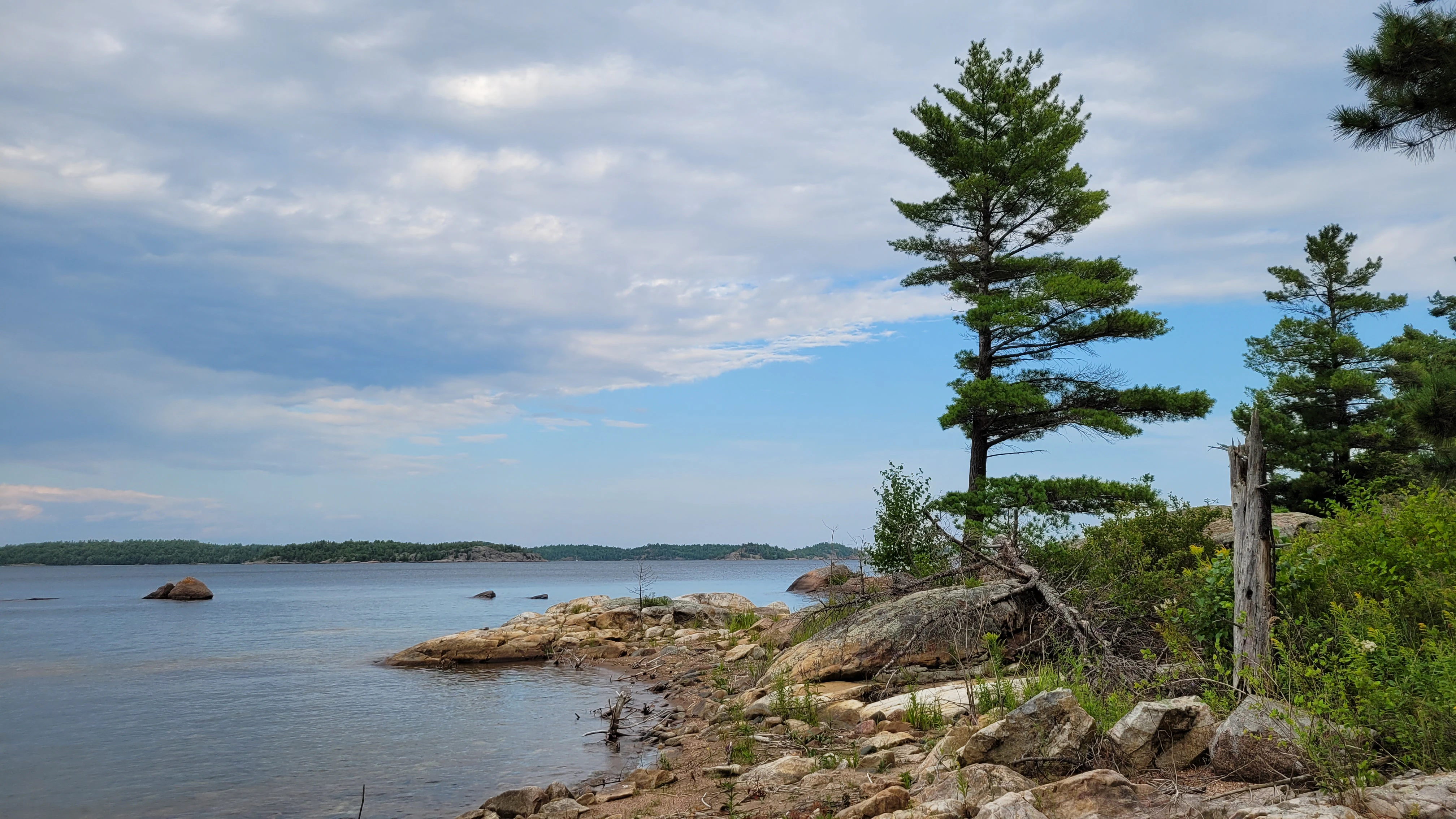 A Sandy beach on North Benjamin Island in Lake Huron, in a protected cove, with rocks, trees and a view of the open waters and islands